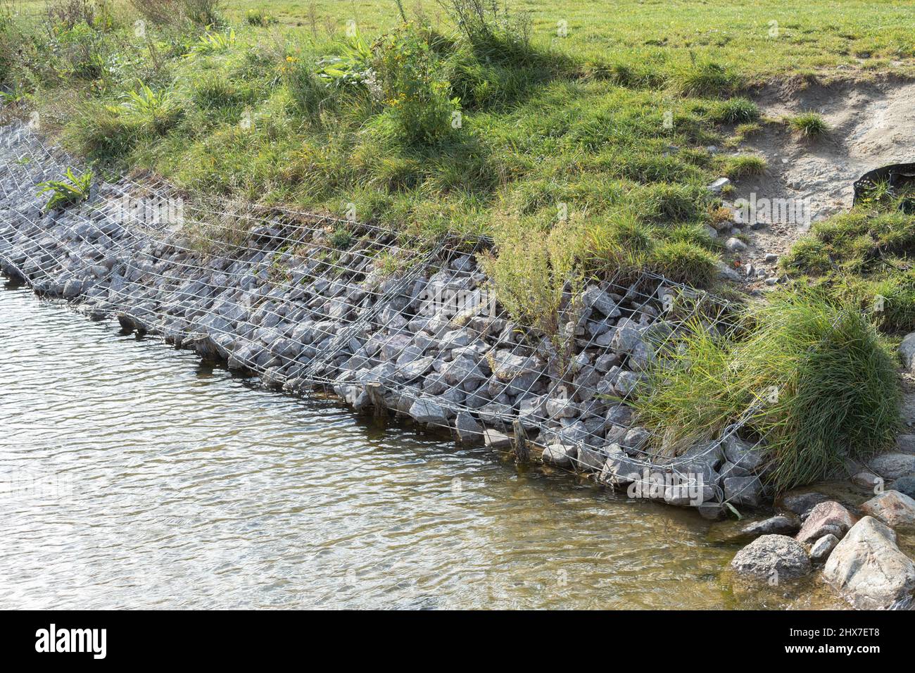 Stärkung der Ufer des Flusses, Mesh und Steine. Landschaft Flussufer und große Steine mit Metallgeflecht Stockfoto