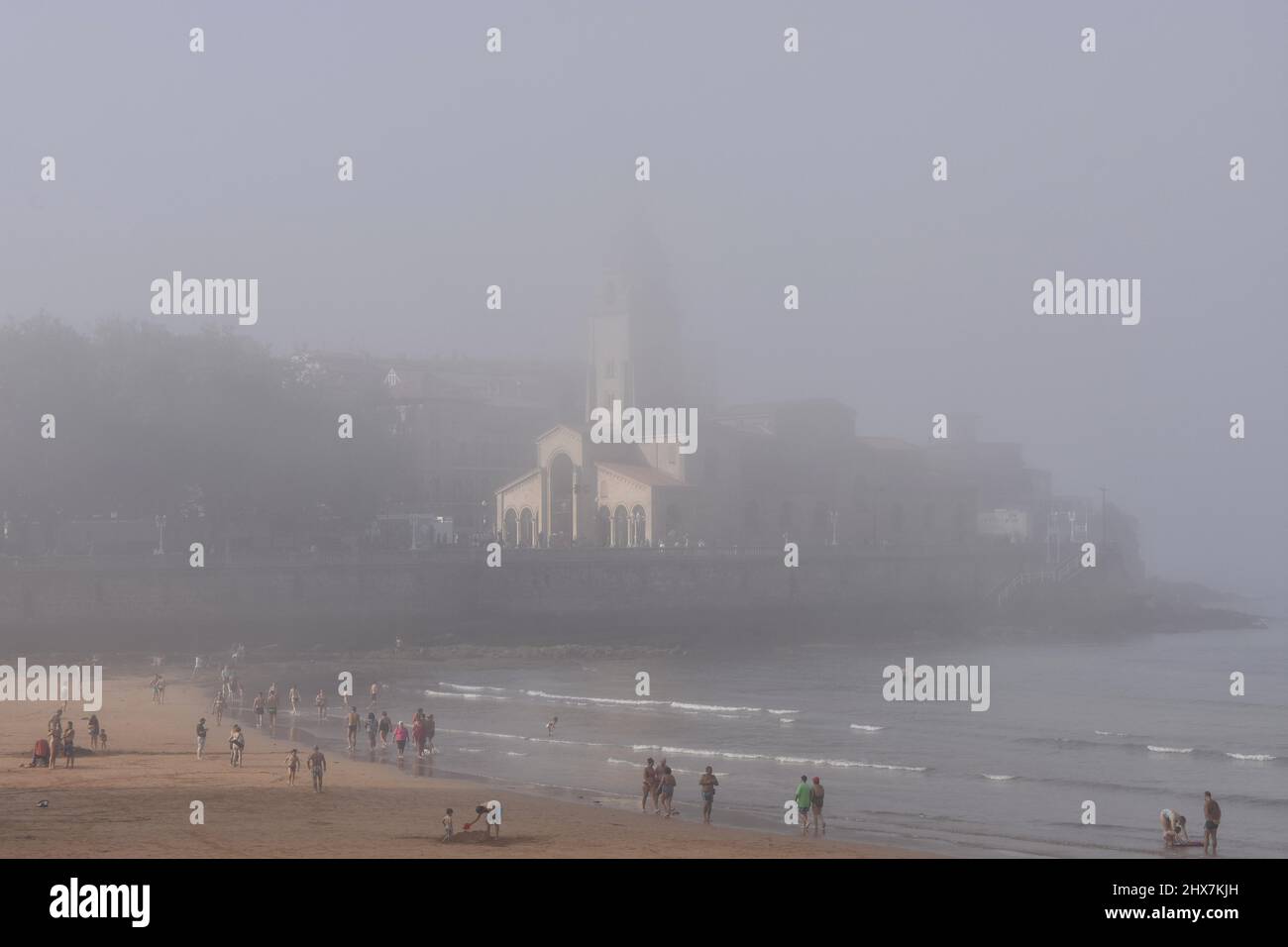 Menschen Urlauber am Strand Playa de San Lorenzo mit Kirche San Pedro im Hintergrund. Nebliger Sommernachmittag in Gijon Asturias Spanien. Stockfoto