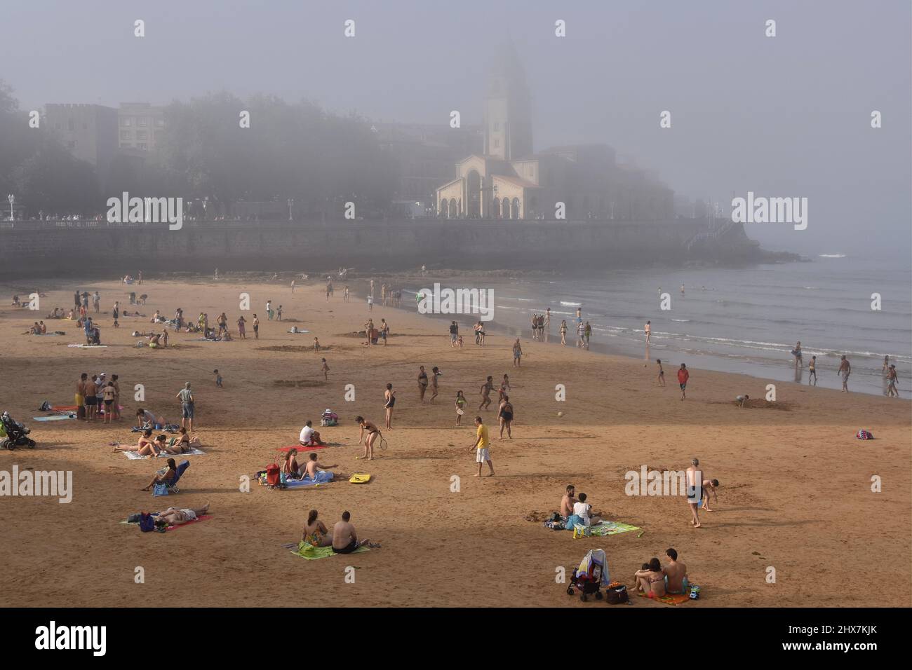 Menschen Urlauber am Strand Playa de San Lorenzo mit Kirche San Pedro im Hintergrund. Nebliger Sommernachmittag in Gijon Asturias Spanien. Stockfoto