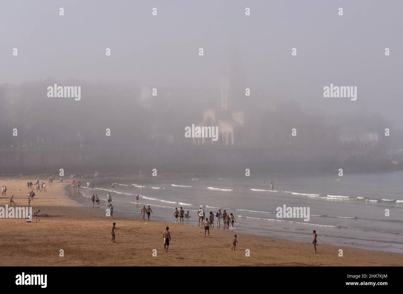 Menschen Urlauber am Strand Playa de San Lorenzo mit Kirche San Pedro im Hintergrund. Nebliger Sommernachmittag in Gijon Asturias Spanien. Stockfoto