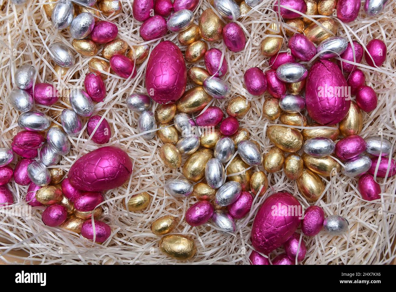 Stapel von bunten, blassen Pastellfolie umwickelten schokoladenöstereiern in Rosa, Silber und Gold auf einem blaßgefürchteten Rahmennest. Stockfoto