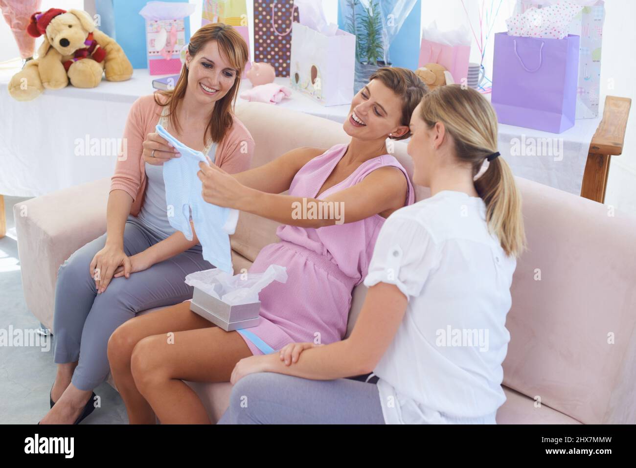 Auf jeden Fall ein Junge. Eine Schwangerin hält die Kleidung der kleinen Jungen an ihrer Babydusche aus. Stockfoto