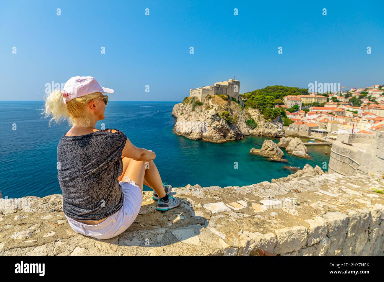 Frau, die auf den oberen Wänden der Stadt Dubrovnik in Kroatien ruht. Blick auf die Festung Fort Lovrijenac, über den Westhafen. Dubrovnik historische Stadt von Kroatien Stockfoto