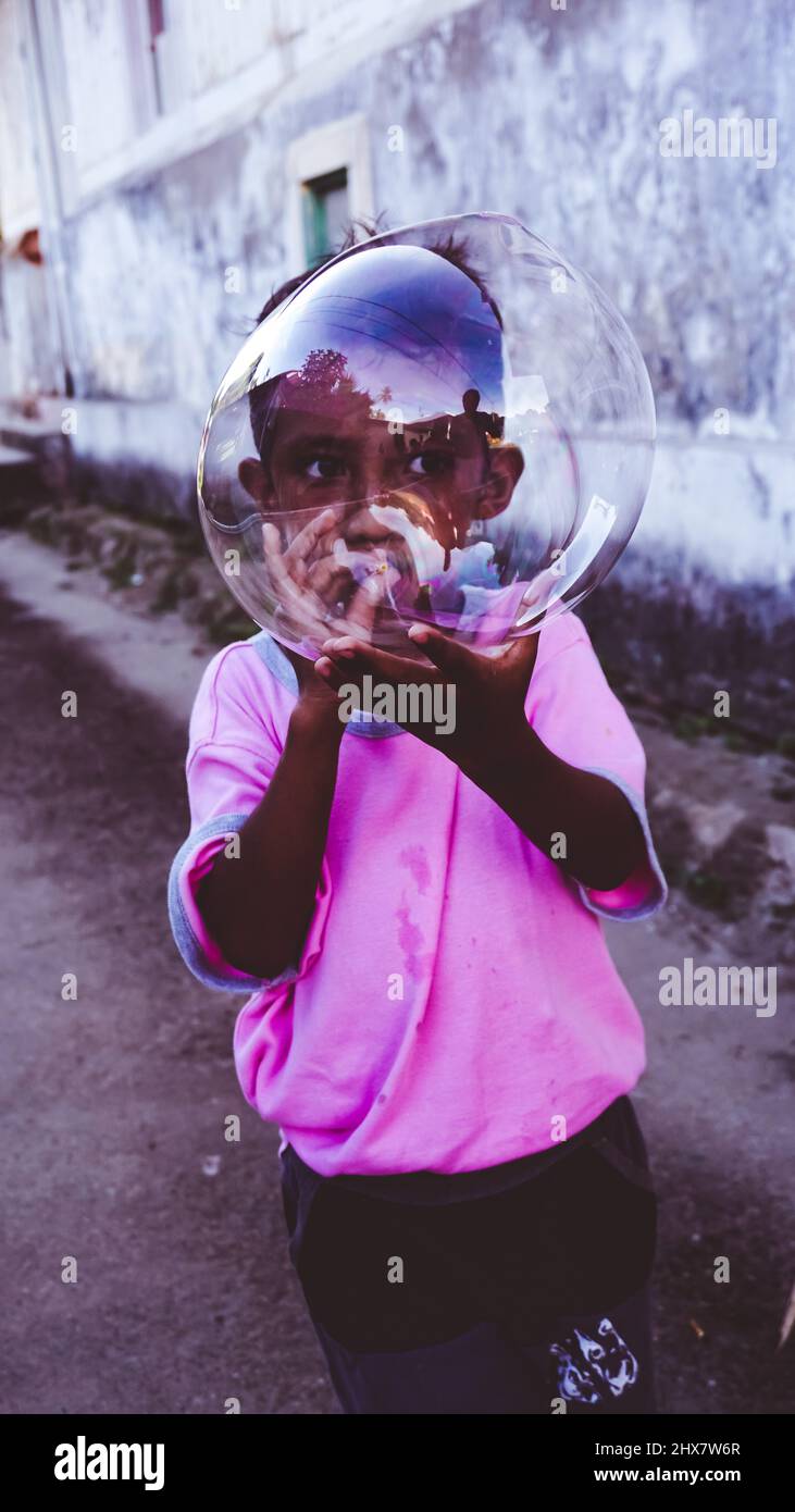 Ein kleines Kind spielt tagsüber mit einem aufblasbaren Ballon mitten auf der Straße in einem Dorf in Ambon, das Dorf heißt Hatalai Stockfoto