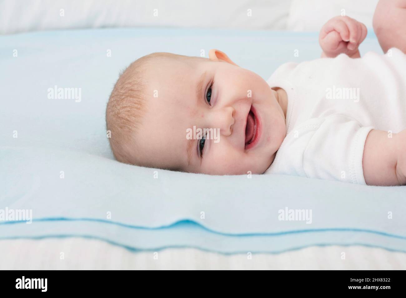 Kleines Mädchen, das sich auf eine blaue Decke legt, Kopf zur Seite gedreht, lachend, Nahaufnahme Stockfoto