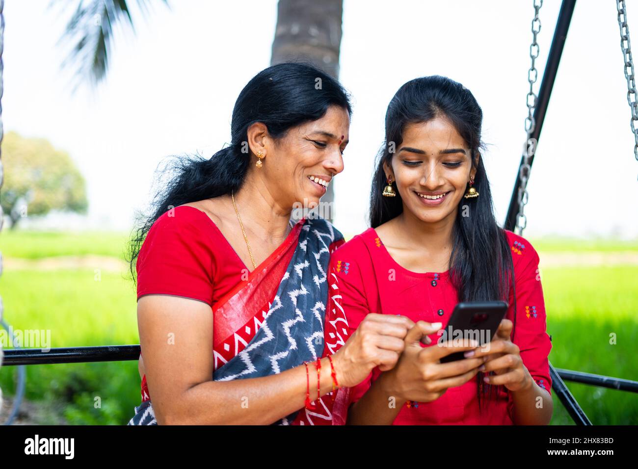 Entspannte Mutter und Tochter auf Schaukel mit Handy - Konzept von Glück, Bindung, Social Media und indische Familie Stockfoto