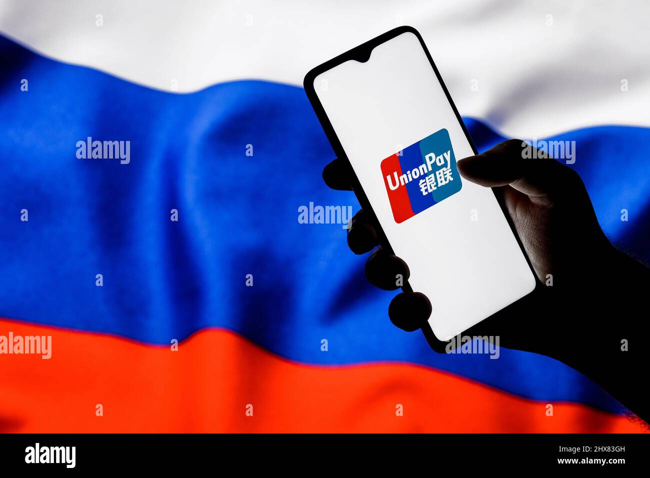 UnionPay ist ein chinesisches elektronisches Geldtransfersystem weltweit. UnionPay-Logo auf dem Smartphone-Bildschirm in der Hand auf dem Hintergrund der Russland-Flagge. Stockfoto