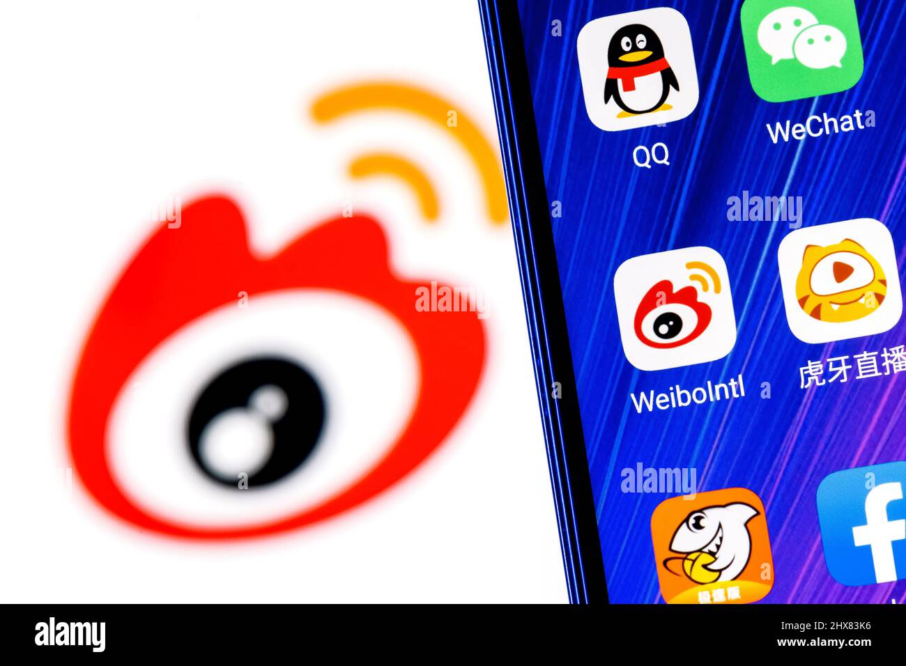 Das Symbol der chinesischen Microblogging-Service-Anwendung Weibo unter anderem auf dem Smartphone-Bildschirm. Auf dem Hintergrund ist das Weibo-Logo zu sehen. Stockfoto