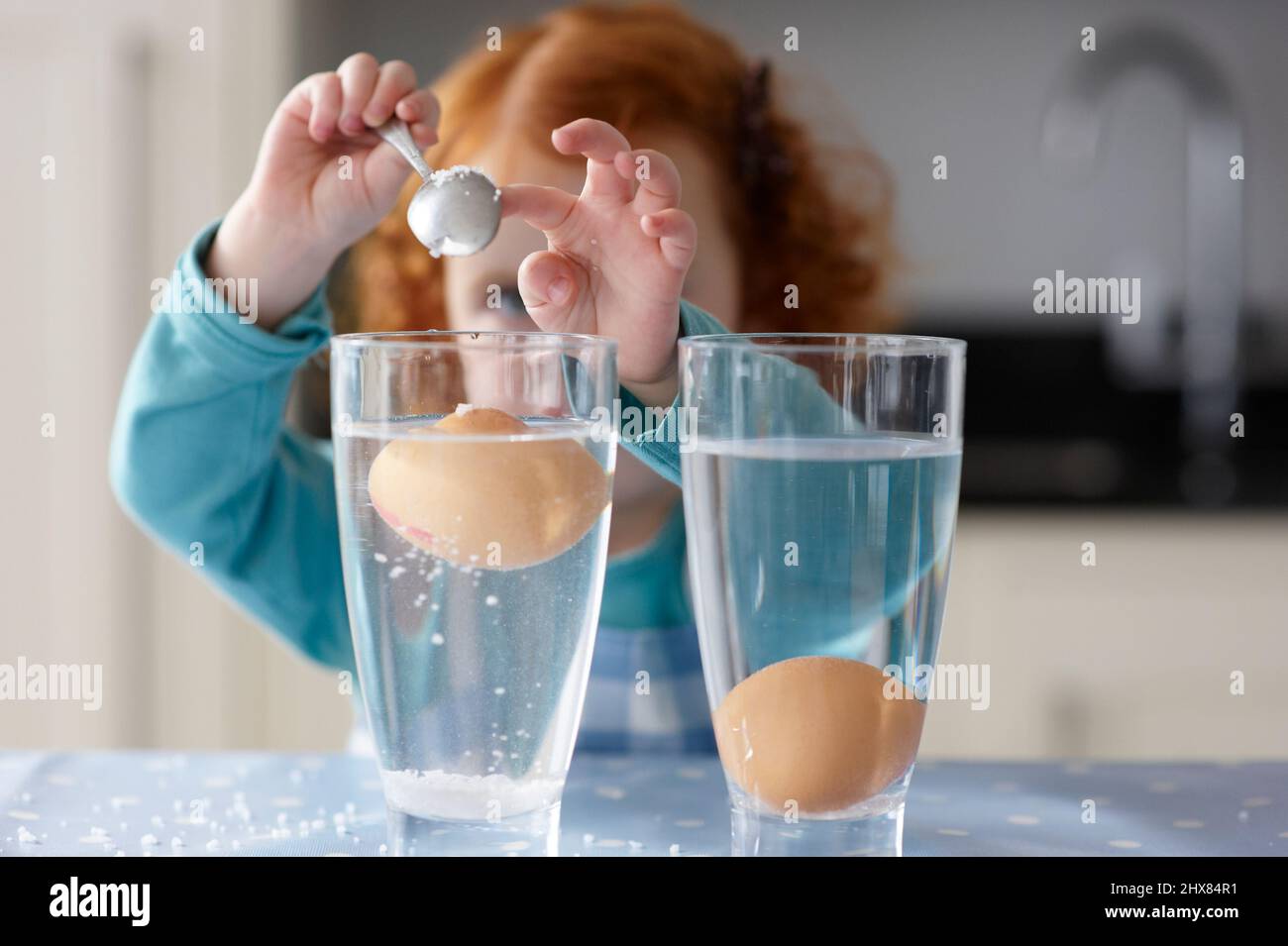 Eier im Glas und Mädchen gießen Salz mit Löffel Stockfoto
