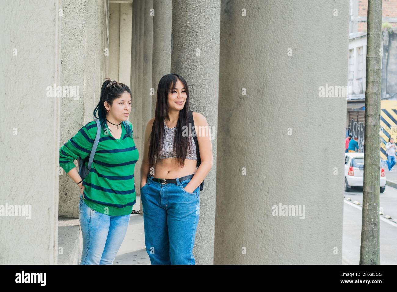 Zwei schöne Latina-Frauen (Freunde), eine kaukasische und die andere braunhäutig, die die Straße entlang gehen, während sie andere Menschen beobachten und kritisieren. Stockfoto