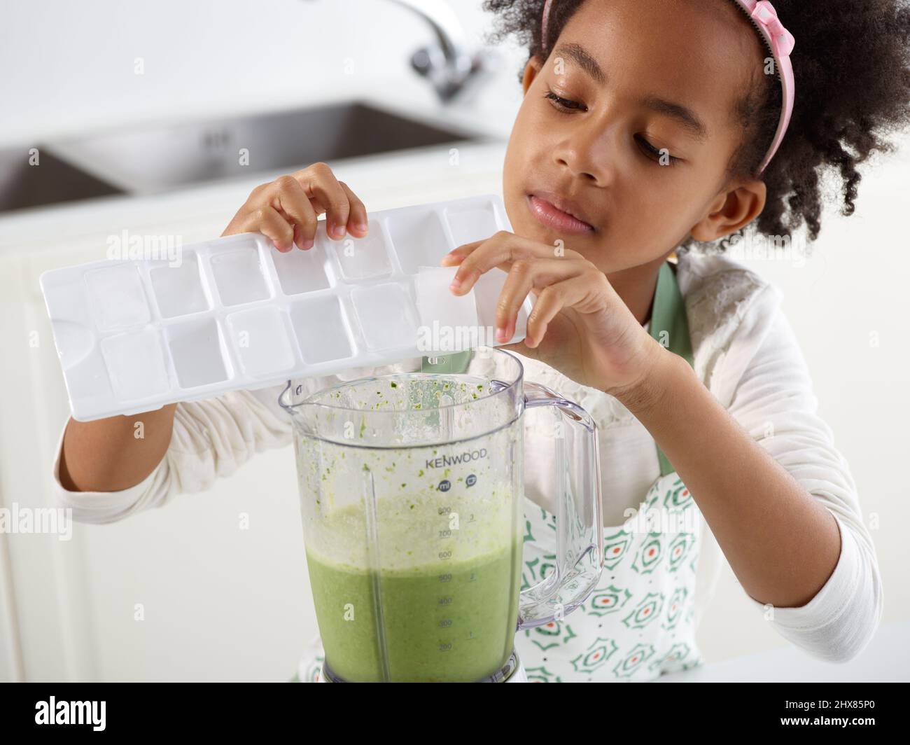 Grüner Smoothie – Hinzufügen von Eis zu einem Mixer, der mit grünem Smoothie gefüllt ist (Schritt 3 von 3) Stockfoto