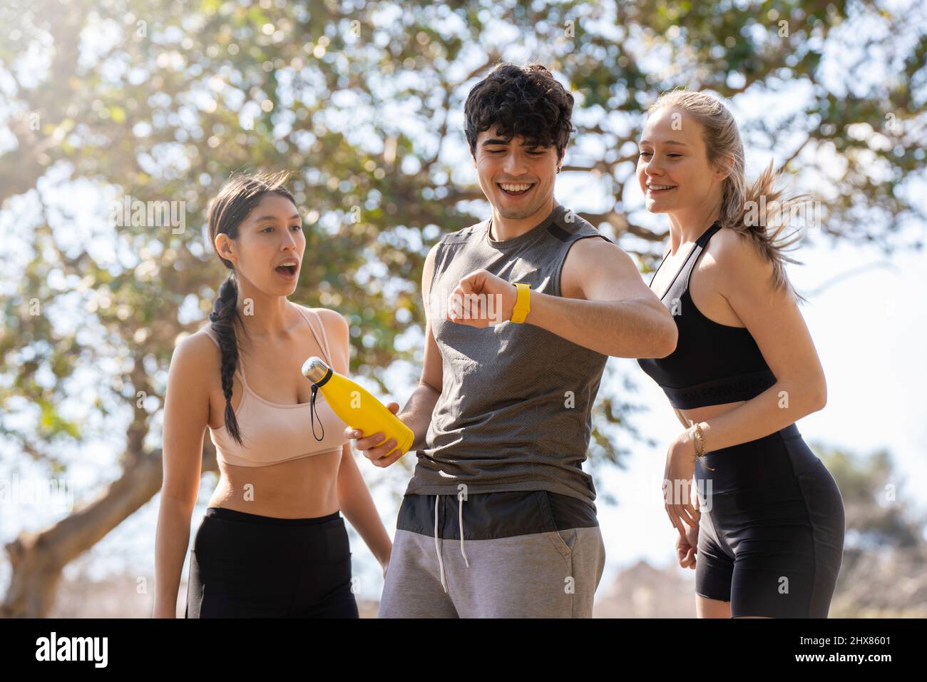 Drei junge Sportbegeisterte schauen sich die smarte Uhr an und lachen im Park Stockfoto