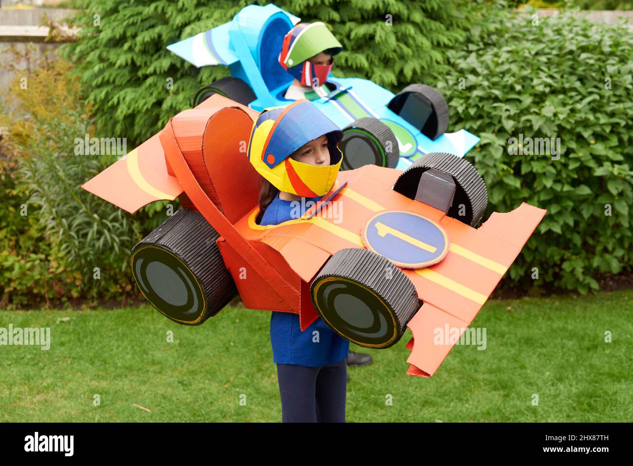 Kinder tragen Rennwagen-Modelle/Kostüm aus Pappe, spielen im Garten Stockfoto