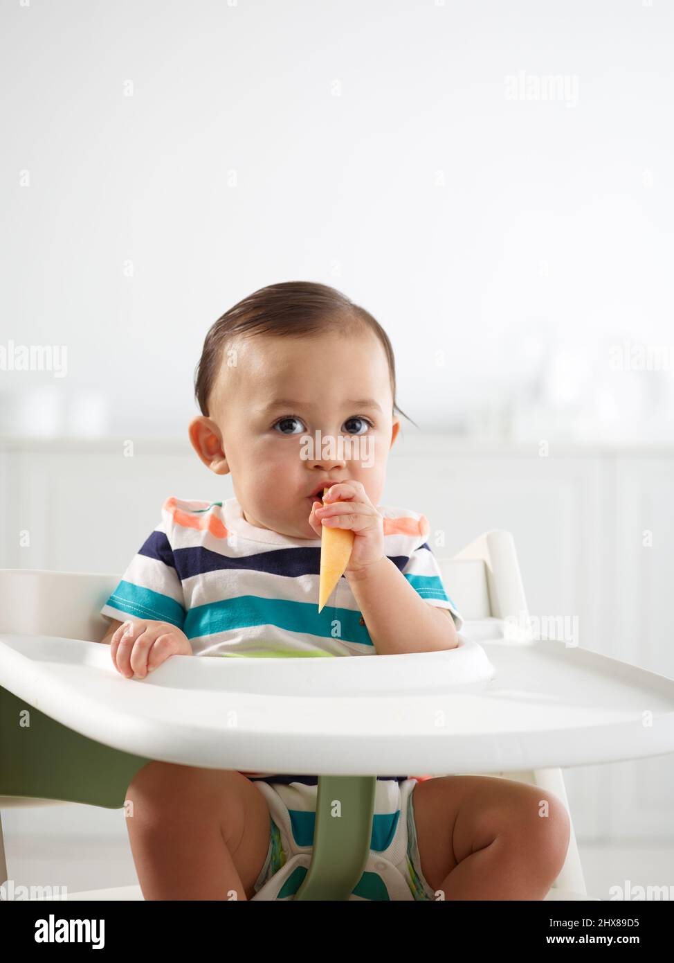 Baby im Alter von 10 Monaten essen im Hochstuhl Stockfoto