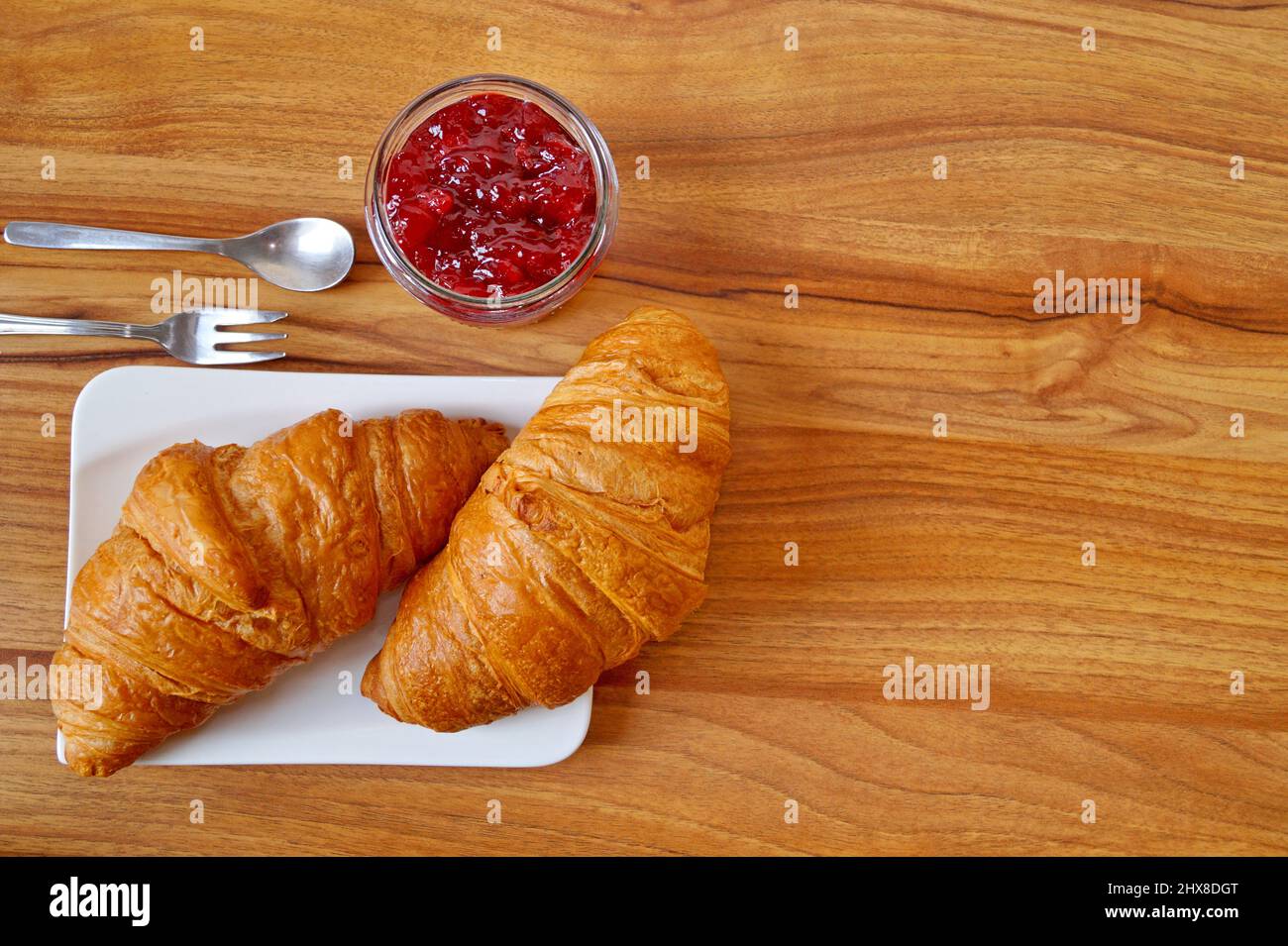 Zwei Croissants liegen auf einem weißen Teller neben einem Glas mit Beerenmarmelade. Das Foto ist quadratisch. Stockfoto