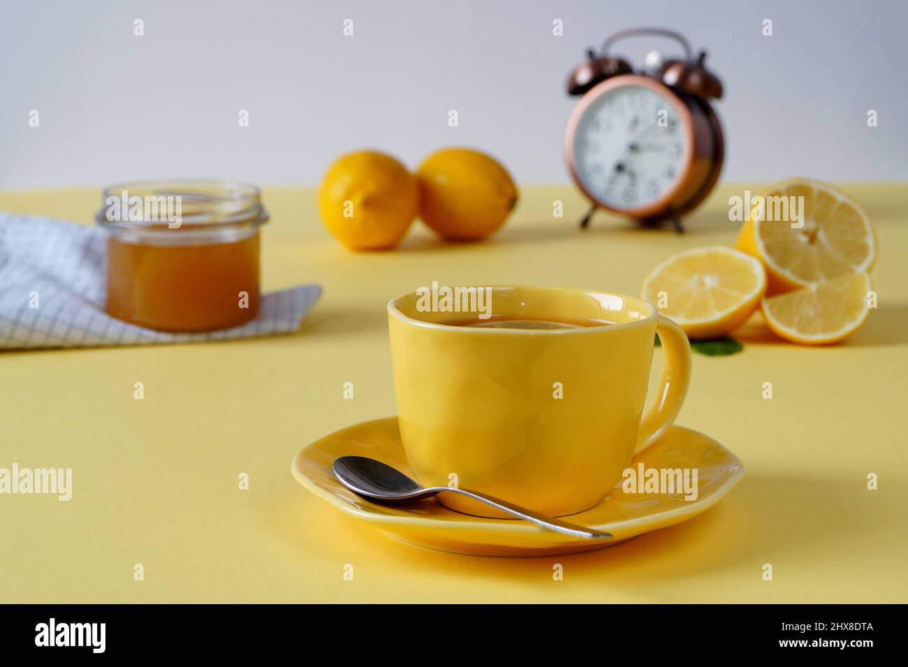 Frühstück: Warmes Getränk mit Honig oder Marmelade auf gelbem Hintergrund. Im Hintergrund befindet sich ein Wecker, der die Morgenzeit - 7 Stunden anzeigt Stockfoto