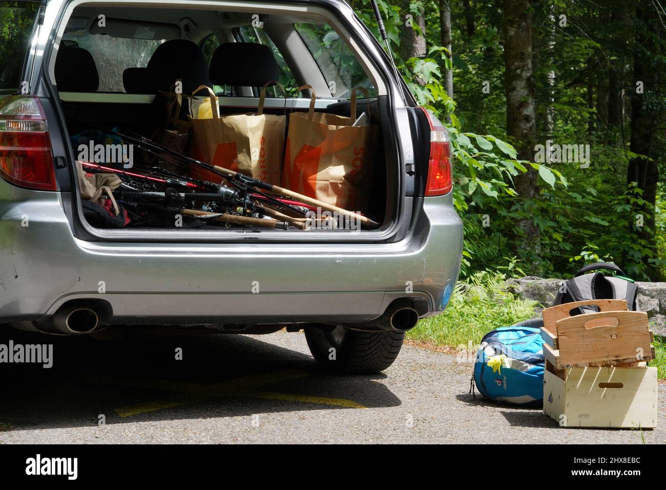 Gepäckraum eines Autos voller Angelausrüstung. Es gibt einige Rucksäcke und Holzkisten außerhalb des Autos auf dem Boden platziert. Stockfoto
