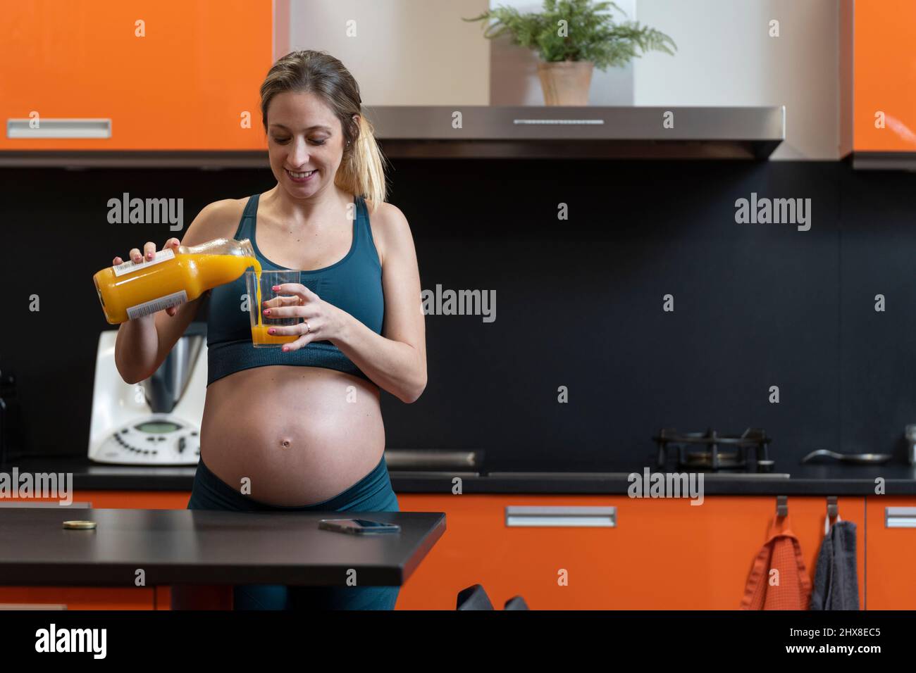 Schwanger blonde Frau trinken einen Orangensaft in der Küche Stockfoto