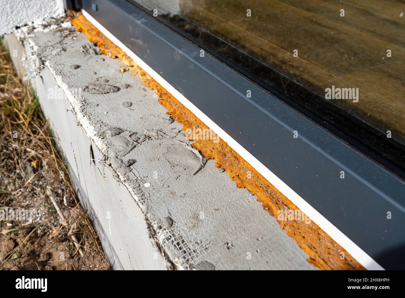 Alter vergilbter Montageschaum unter einem großen Terrassenfenster, sichtbares Styropor, das die Fundamente des Hauses isoliert. Stockfoto