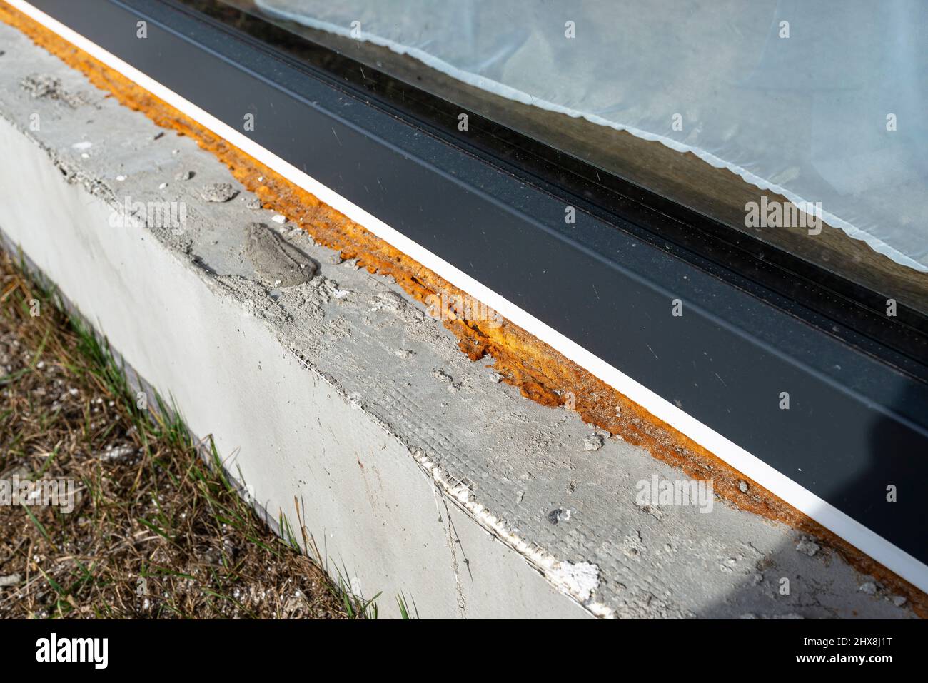 Alter vergilbter Montageschaum unter einem großen Terrassenfenster, sichtbares Styropor, das die Fundamente des Hauses isoliert. Stockfoto