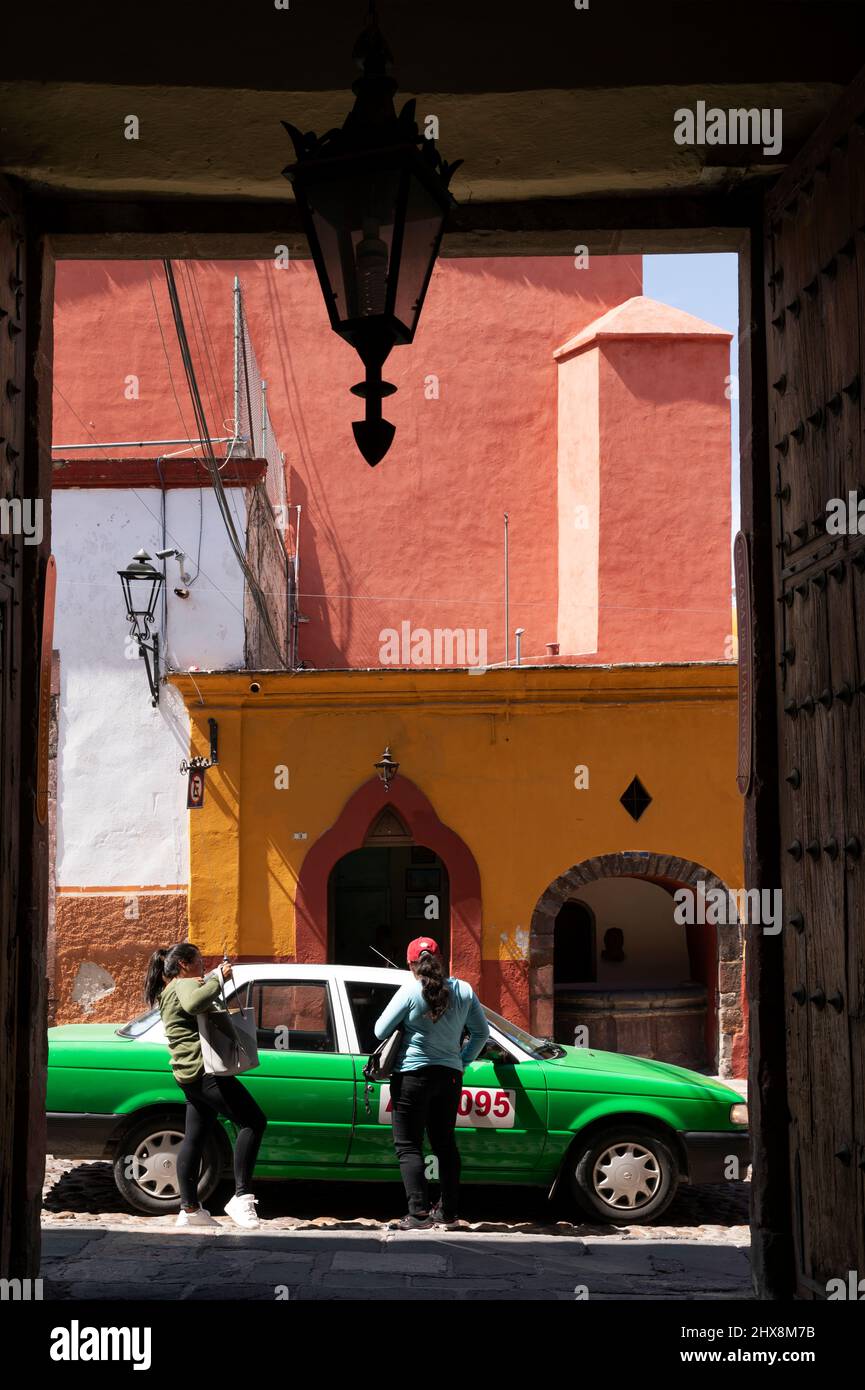 Mexiko, der Staat Guanajuato, San Miguel de Allende, zwei Frauen und ein grünes Taxi, das durch eine Tür gesehen wird Stockfoto