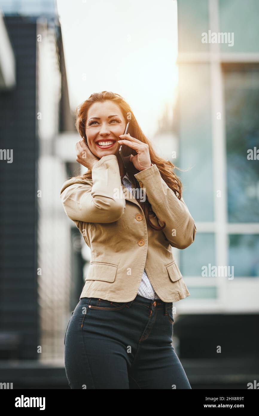 Erfolgreiche junge Frau, die unterwegs mit dem Smartphone vor dem Büroviertel spricht. Stockfoto