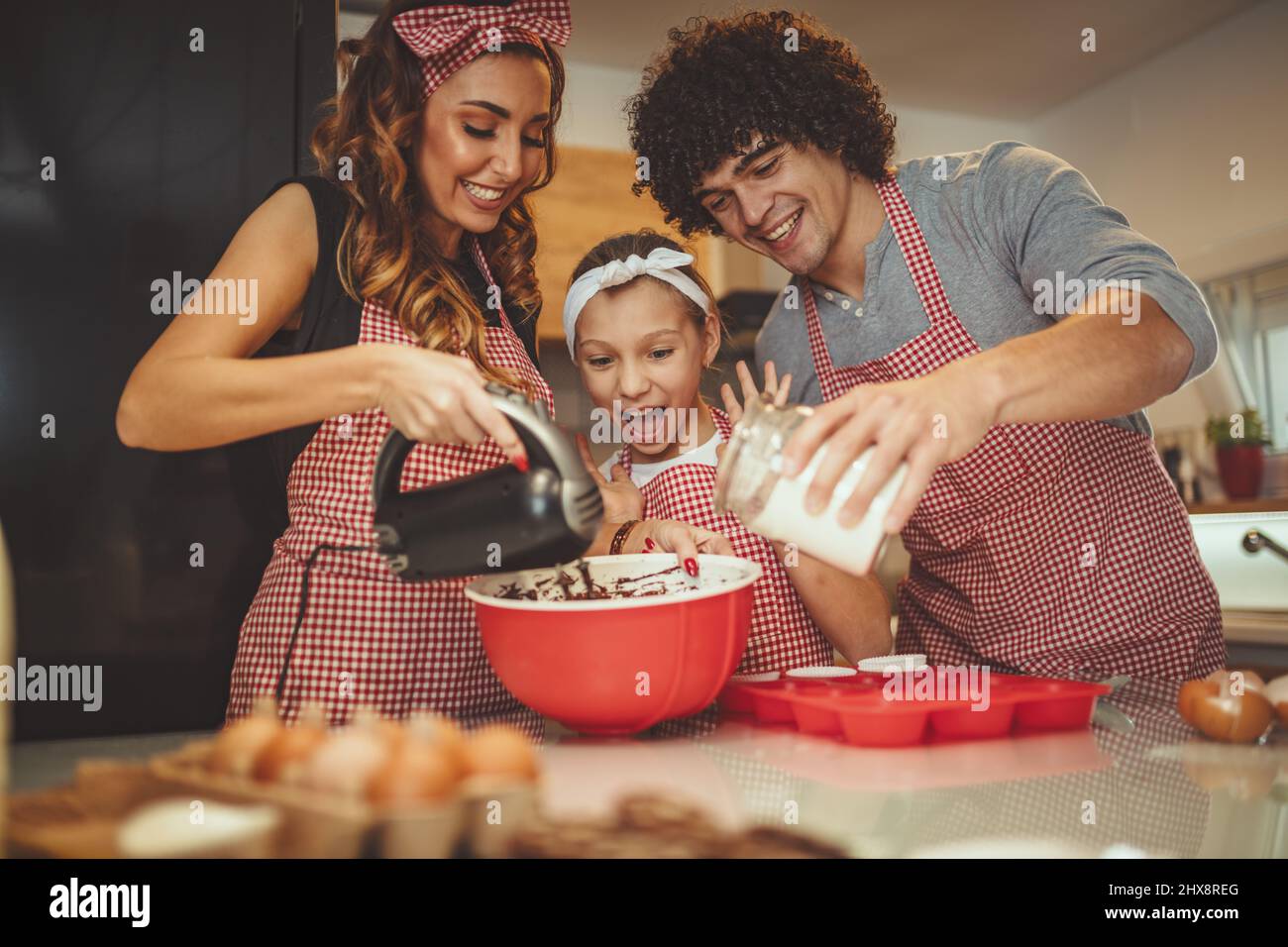 Glückliche Eltern und ihre Tochter sind Cookies gemeinsam in der Küche. Kleines Mädchen hilft, ihre Eltern mischen Teig mit Mixer. Stockfoto