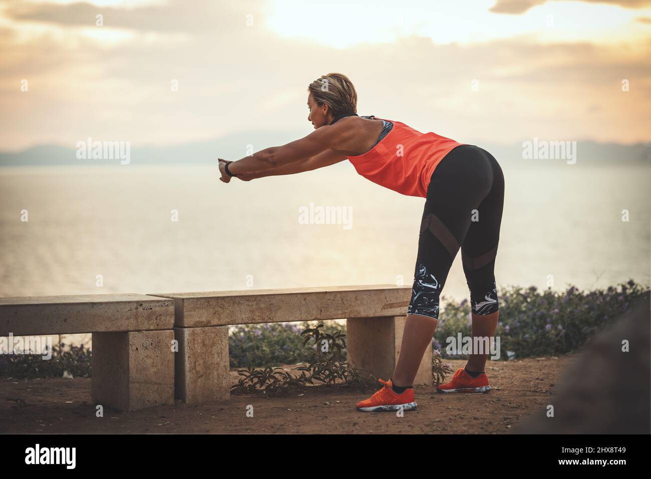 Eine schöne junge Frau macht Stretching-Übungen am Meeresstrand bei Sonnenaufgang. Stockfoto