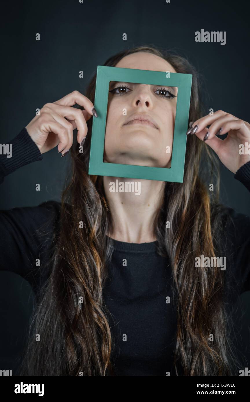 Gerahmte Schönheit - Porträt einer schönen Brünette Frau mit einem kleinen Rahmen vor ihrem Gesicht - Konzept für die Einzigartigkeit und Vielfalt Stockfoto