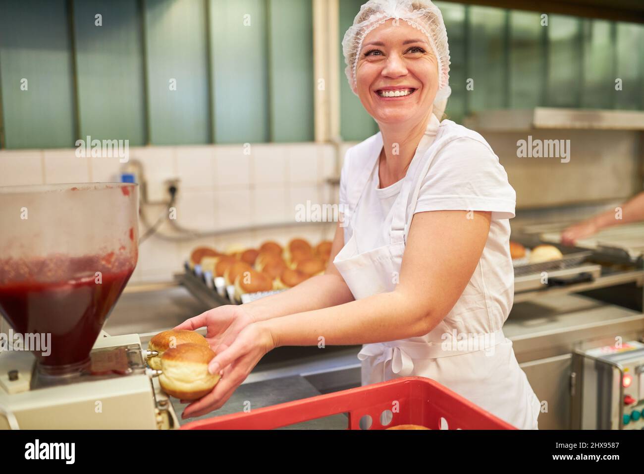 Junge Frau als Bäckerschülerin in der Bäckerei Berliner Pfannkuchen mit Marmelade füllen Stockfoto
