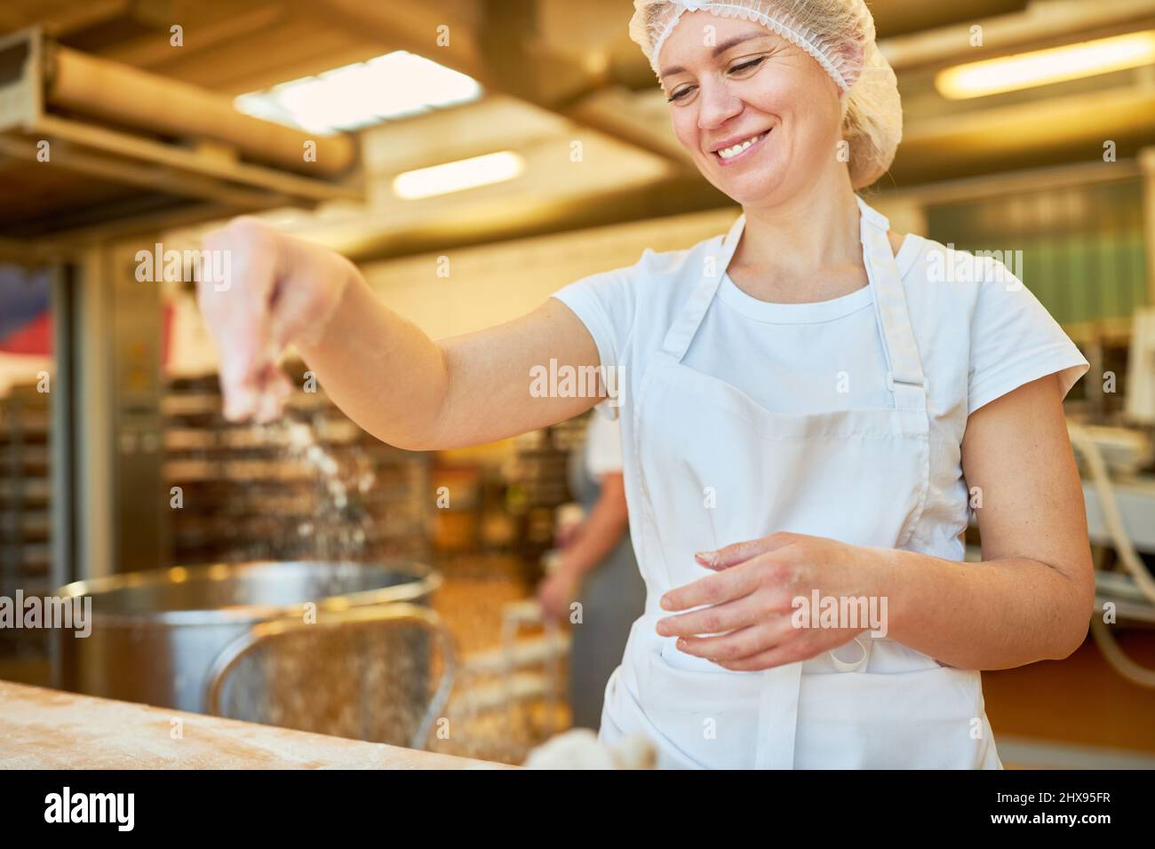 Die Bäckerlehrling streut Mehl in Teig, um das Backen vorzubereiten Stockfoto