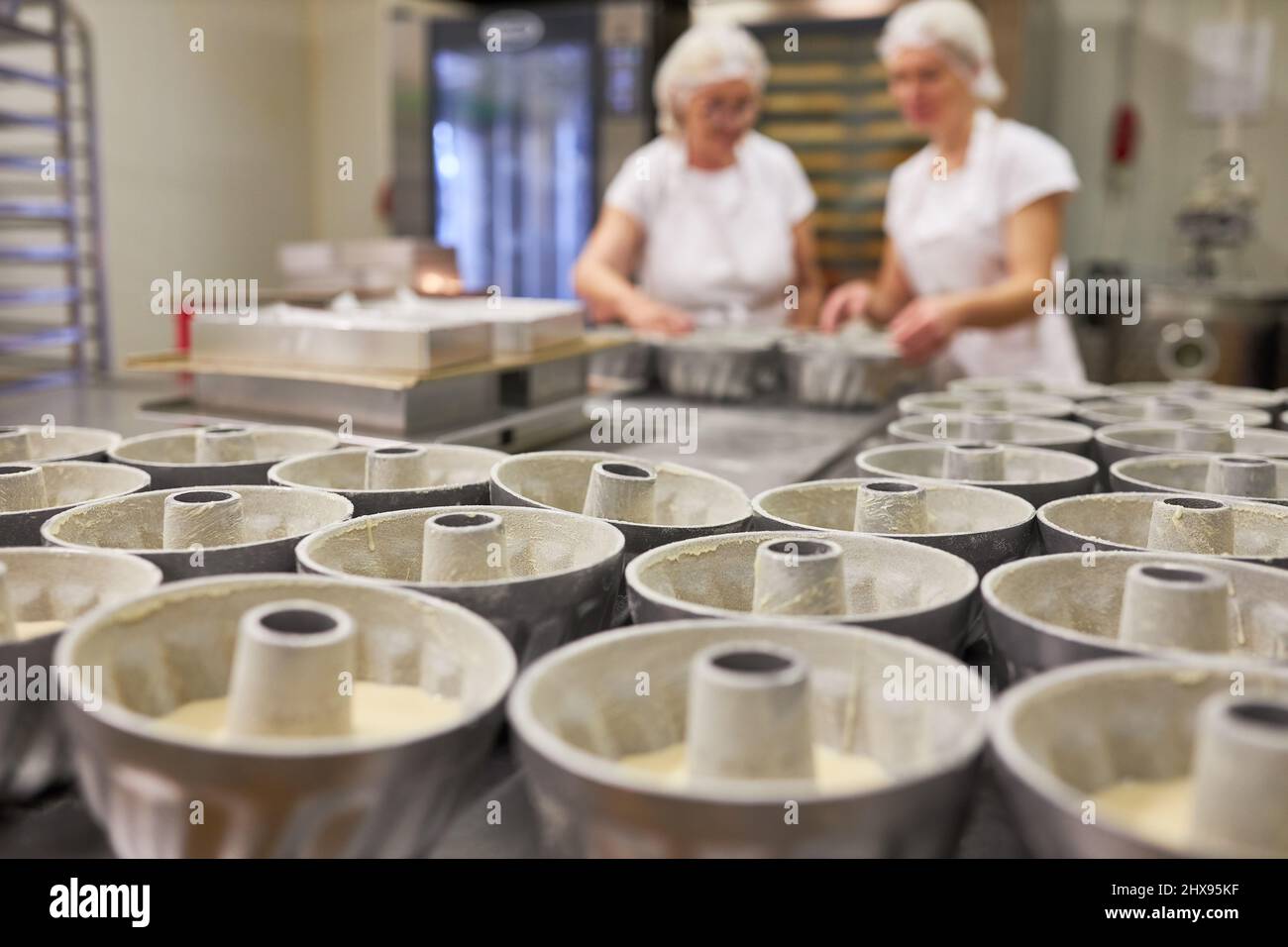 Viele Kuchenformen mit Gugelhupf-Kuchen in einer großen Bäckerei mit einem Backteam im Hintergrund Stockfoto