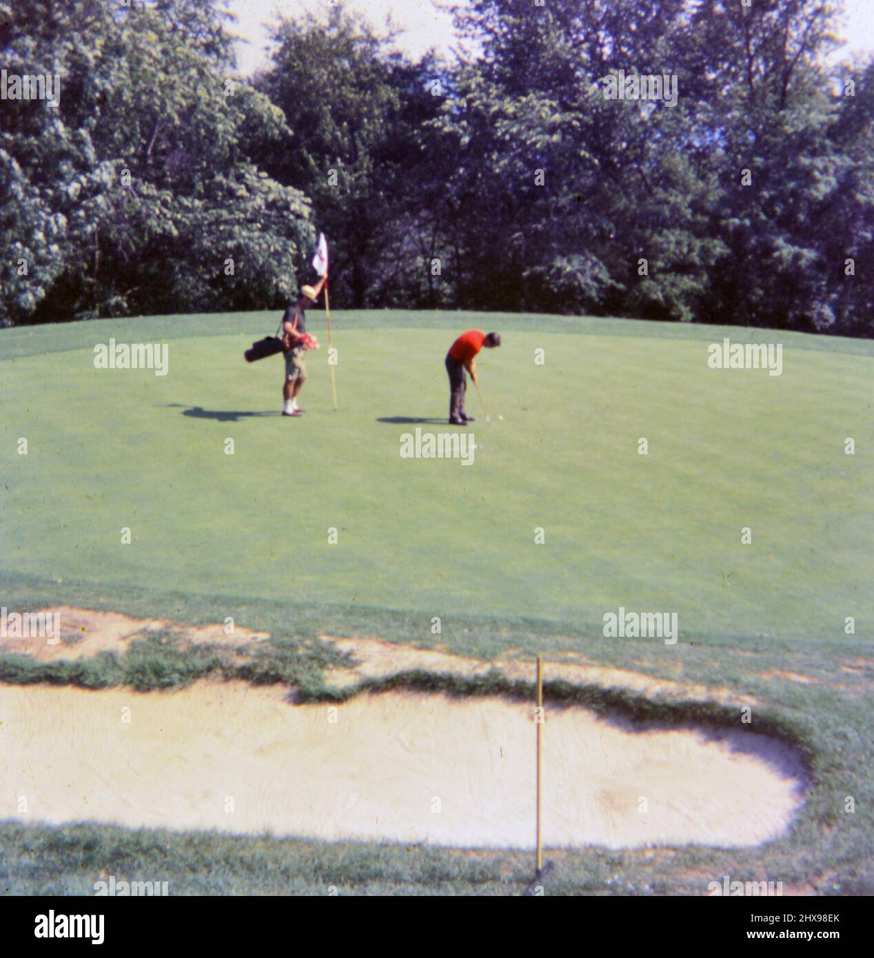 Mann, der Golf spielt, einen Ball auf eine grüne Ca. 1968 Stockfoto