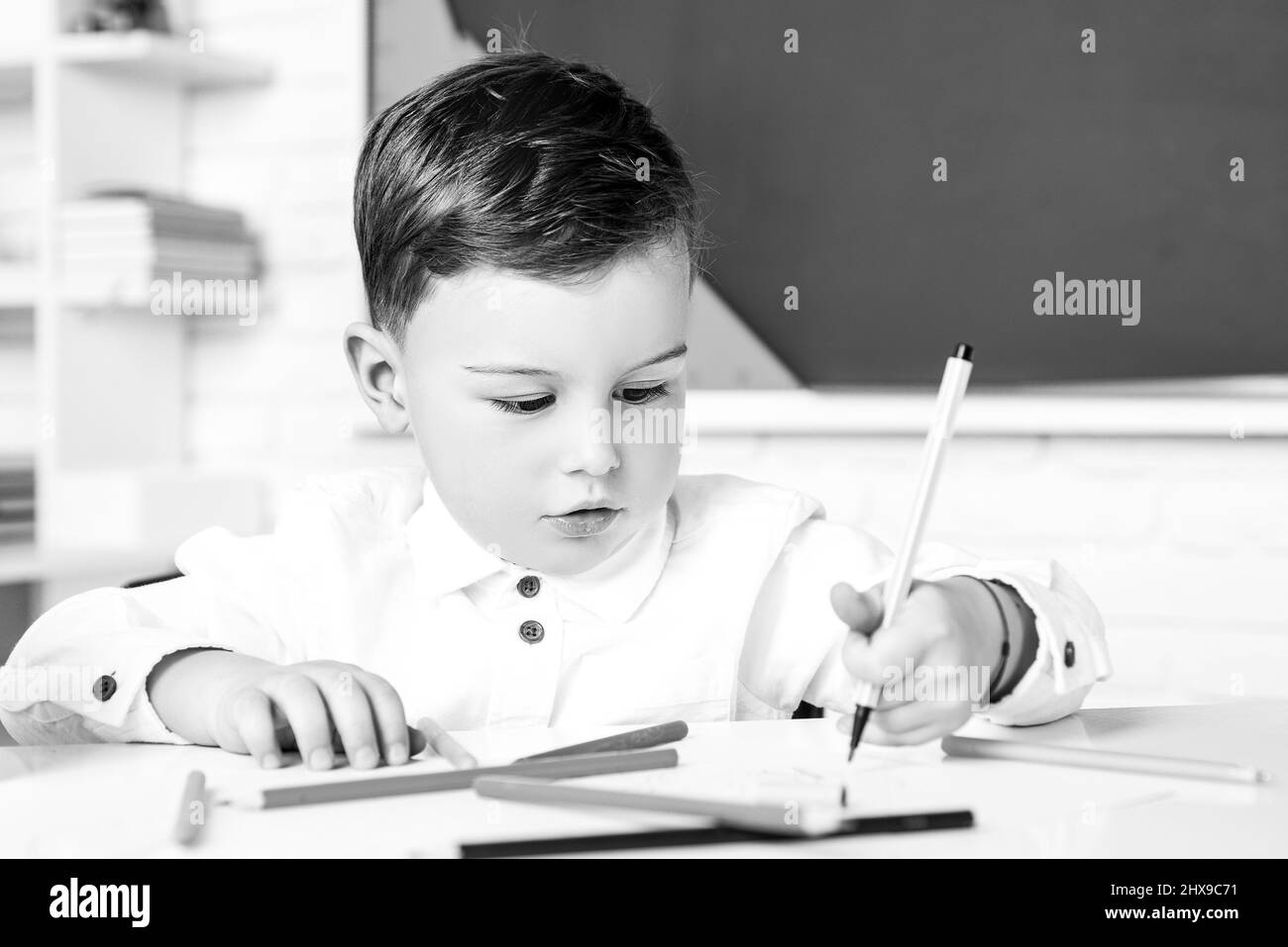 Konzentriertes niedliches Kind, Schreiben im Notizbuch mit Bleistift. Nettes Kind sitzt an einem Schreibtisch drinnen. Stockfoto