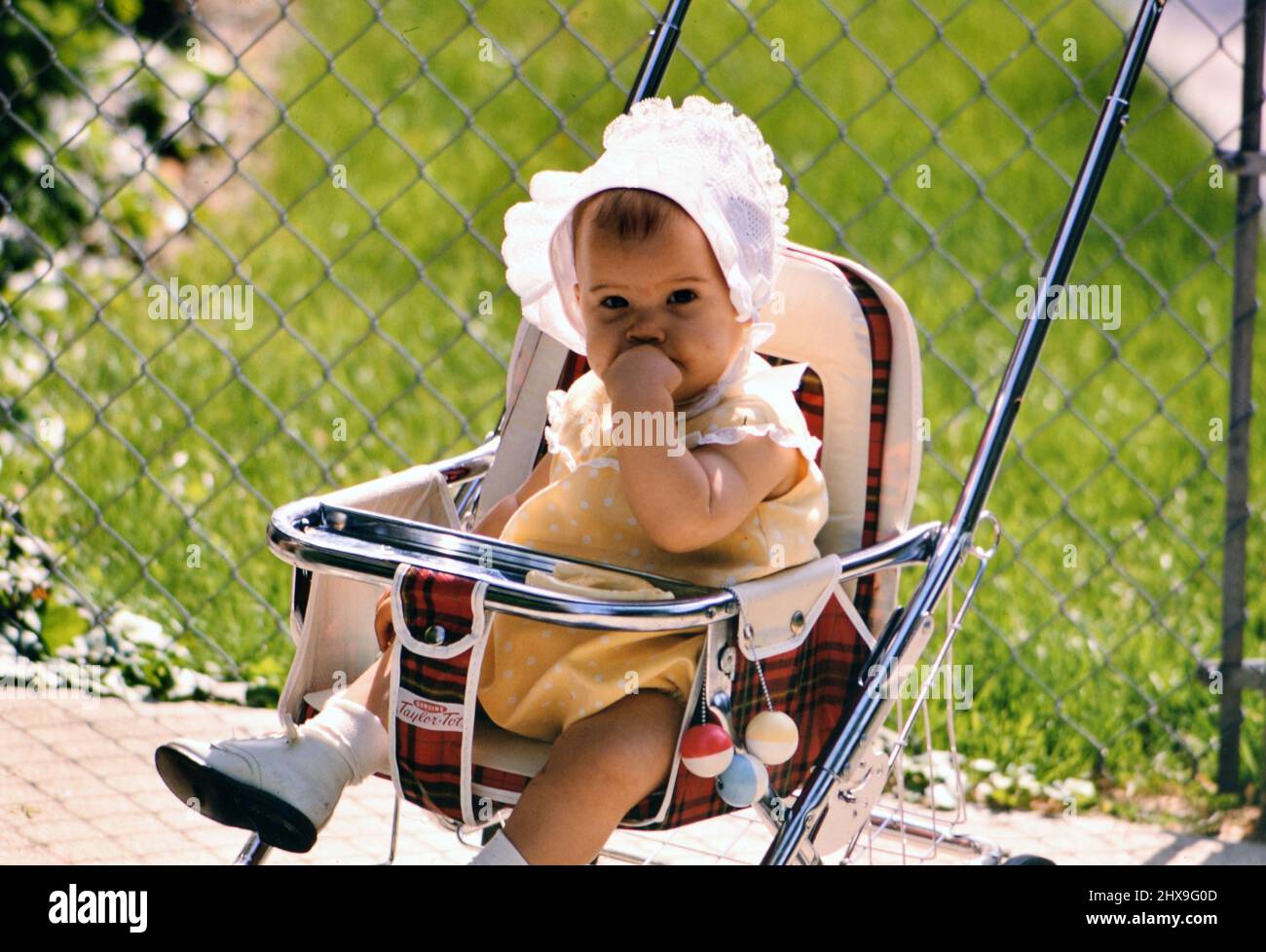 Ein kleines Mädchen, das in einem Kinderwagen sitzt und eine Haube trägt, ca. 1969 Stockfoto