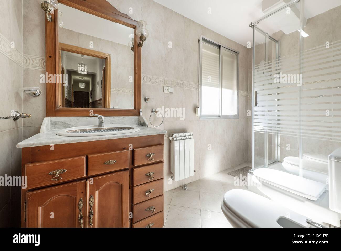 Toilette mit Duschkabine aus Glas, Waschbecken aus weißem Porzellan mit Marmorplatte in einem Holzschrank in der Ferienwohnung Stockfoto