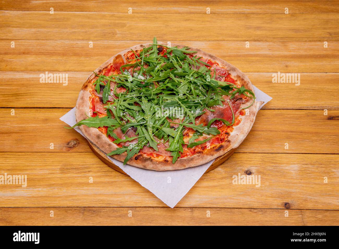 Die Pizza Serrano besteht aus Weizenmehl, Mozzarella-Käse, Tomatenmark, Wasser, serrano-Schinken und geräuchertem Käse auf Backpapier und einem Holzdielentisch Stockfoto