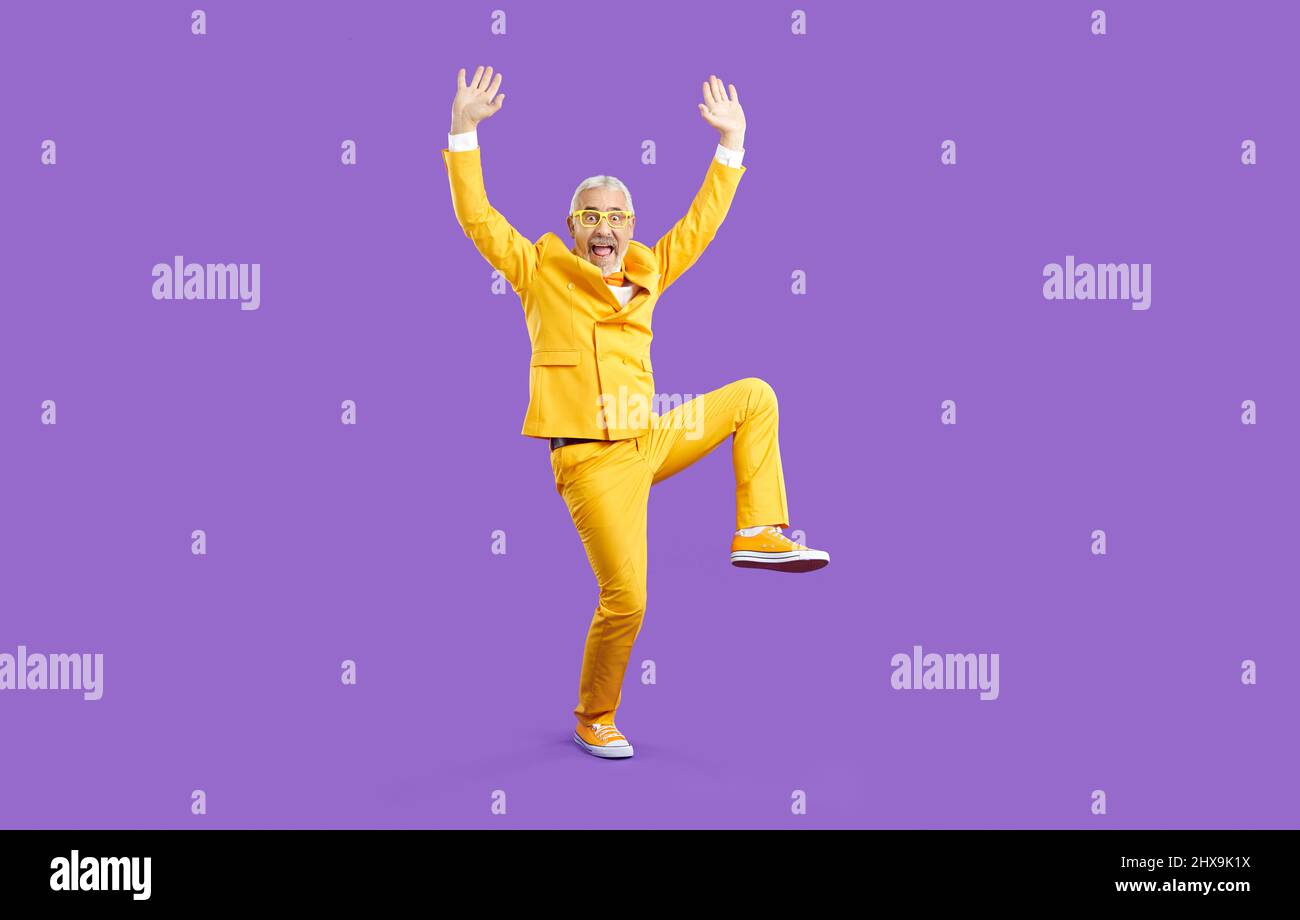 Witziger verrückter älterer Mann in einem gelben Anzug, der im Studio Spaß hat und herumtollt Stockfoto