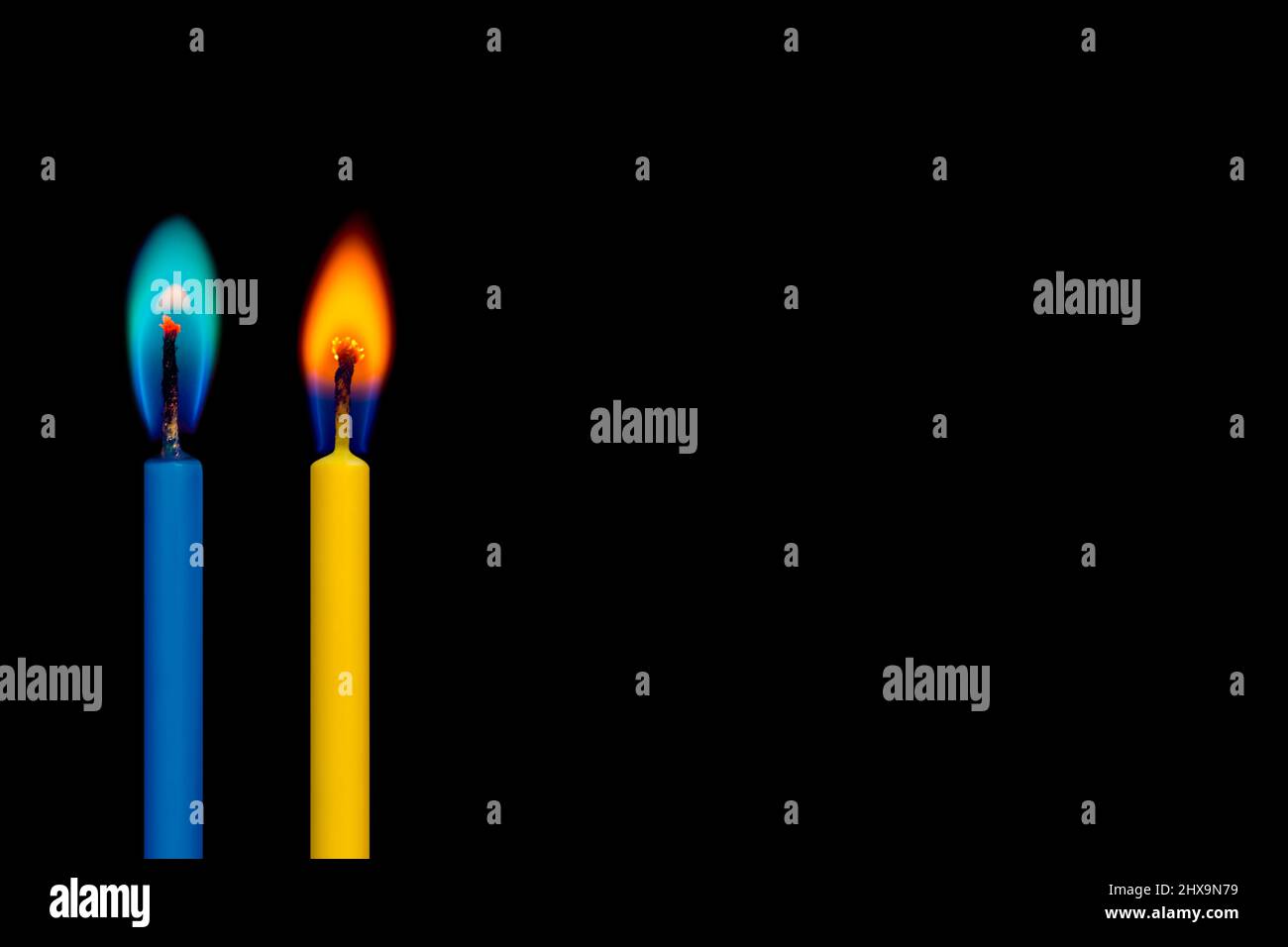 Auf dem schwarzen Hintergrund leuchten zwei blaue und gelbe brennende Kerzen (in ukrainischen Flaggen-Farben) Stockfoto