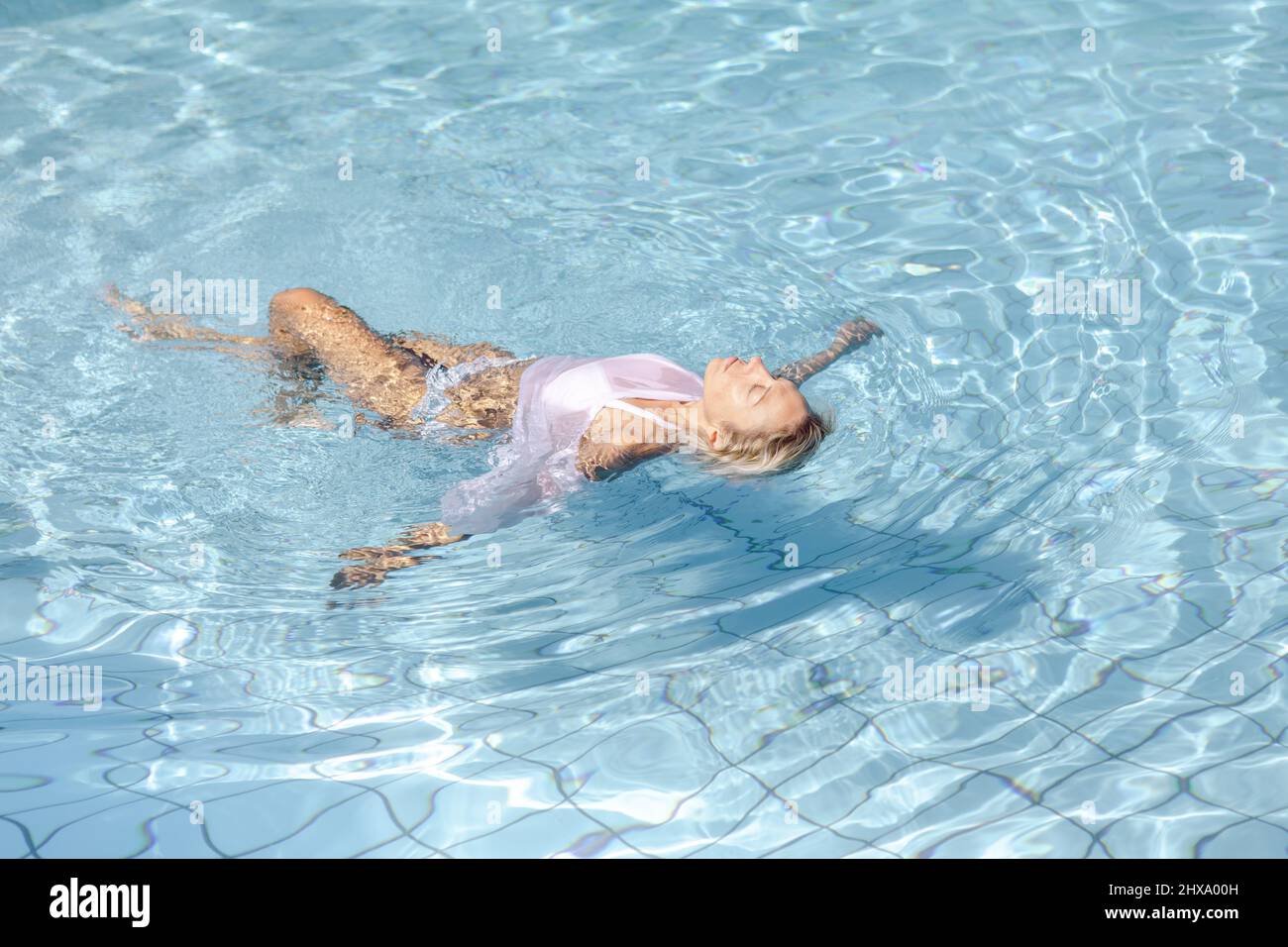 Schöne blonde Frau schwimmt auf ihrem Rücken in einem Pool Stockfoto