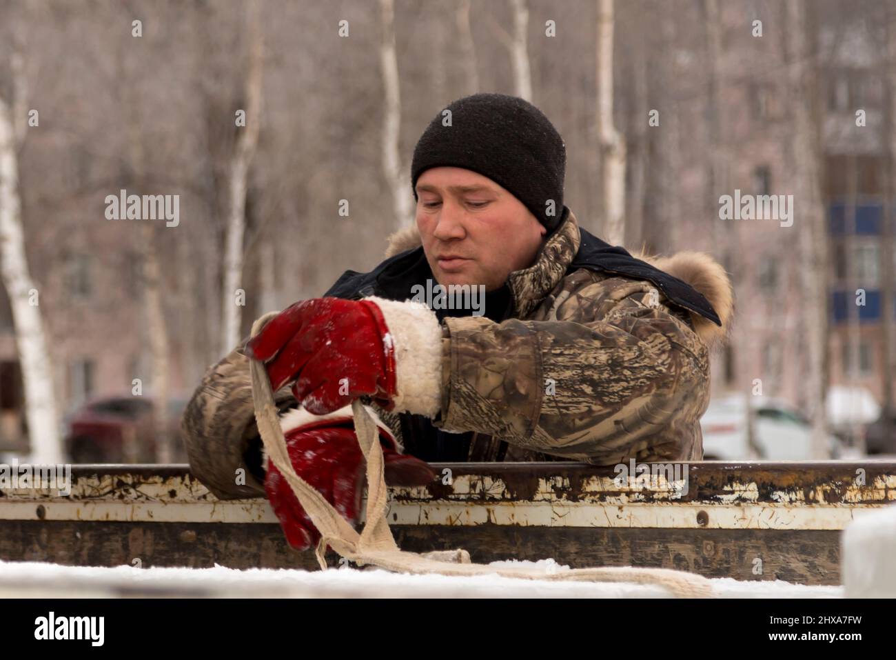 Porträt eines Arbeiters in einer Winterjacke und einem schwarzen Strickmütze mit einem Bandschlinge in den Händen Stockfoto