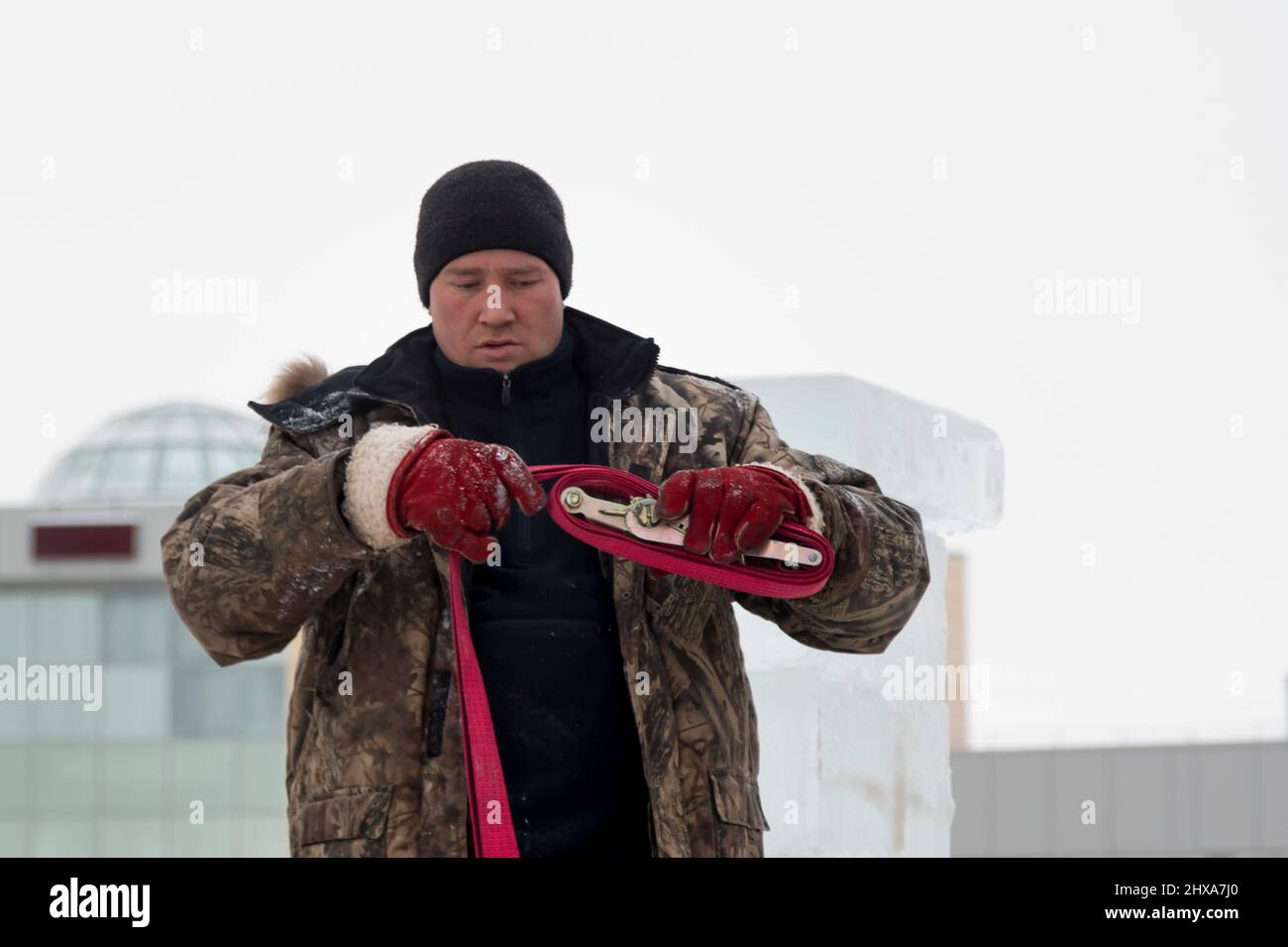 Porträt eines Arbeiters in einer Winterjacke und einem schwarzen Strickmütze mit einem Bandschlinge in den Händen Stockfoto