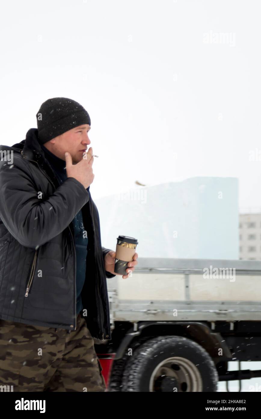 Porträt eines Arbeiters in einem schwarzen Hut mit einem Glas heißen Kaffee in der Hand und einer Zigarette Stockfoto