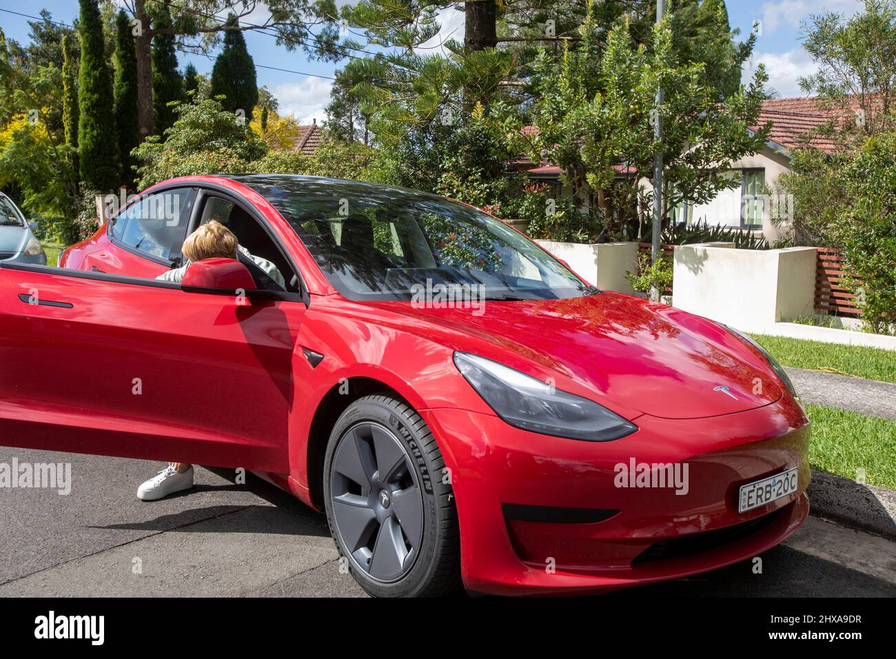 2022 rotes Tesla Modell 3 mit Dame mittleren Alters, Model freigegeben, aus dem Auto treten auf Fahrerseite, Sydney, Australien Stockfoto