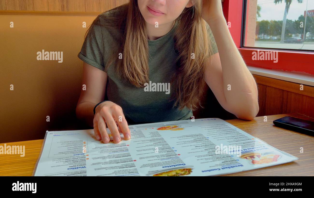 Junge Frau, die das Frühstücksmenü in einem Restaurant - MIAMI, USA - überprüft, 20. FEBRUAR 2022 Stockfoto