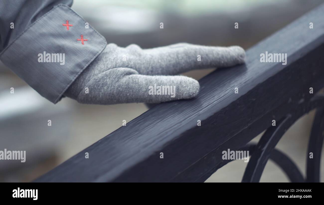 Nahaufnahme der Hand eines jungen Mädchens, die über das Geländer gleitet. Hand in grauem Handschuh berührt Geländer im Freien bei kaltem Wetter. Stockfoto