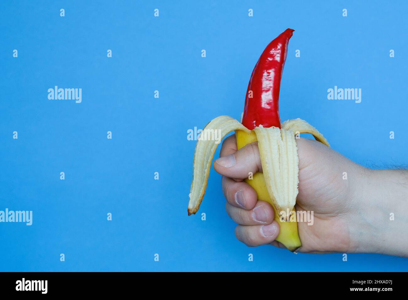 Die Hand hält eine geschälte Banane, aus der roter Pfeffer herausragt. Stockfoto