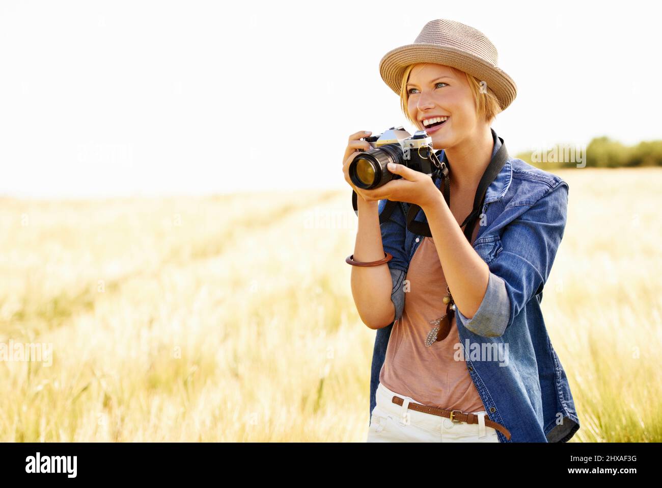 Sie liebt es, die Natur zu fotografieren. Eine attraktive junge Frau, die eine Kamera hält, während sie auf einem Feld unterwegs ist. Stockfoto