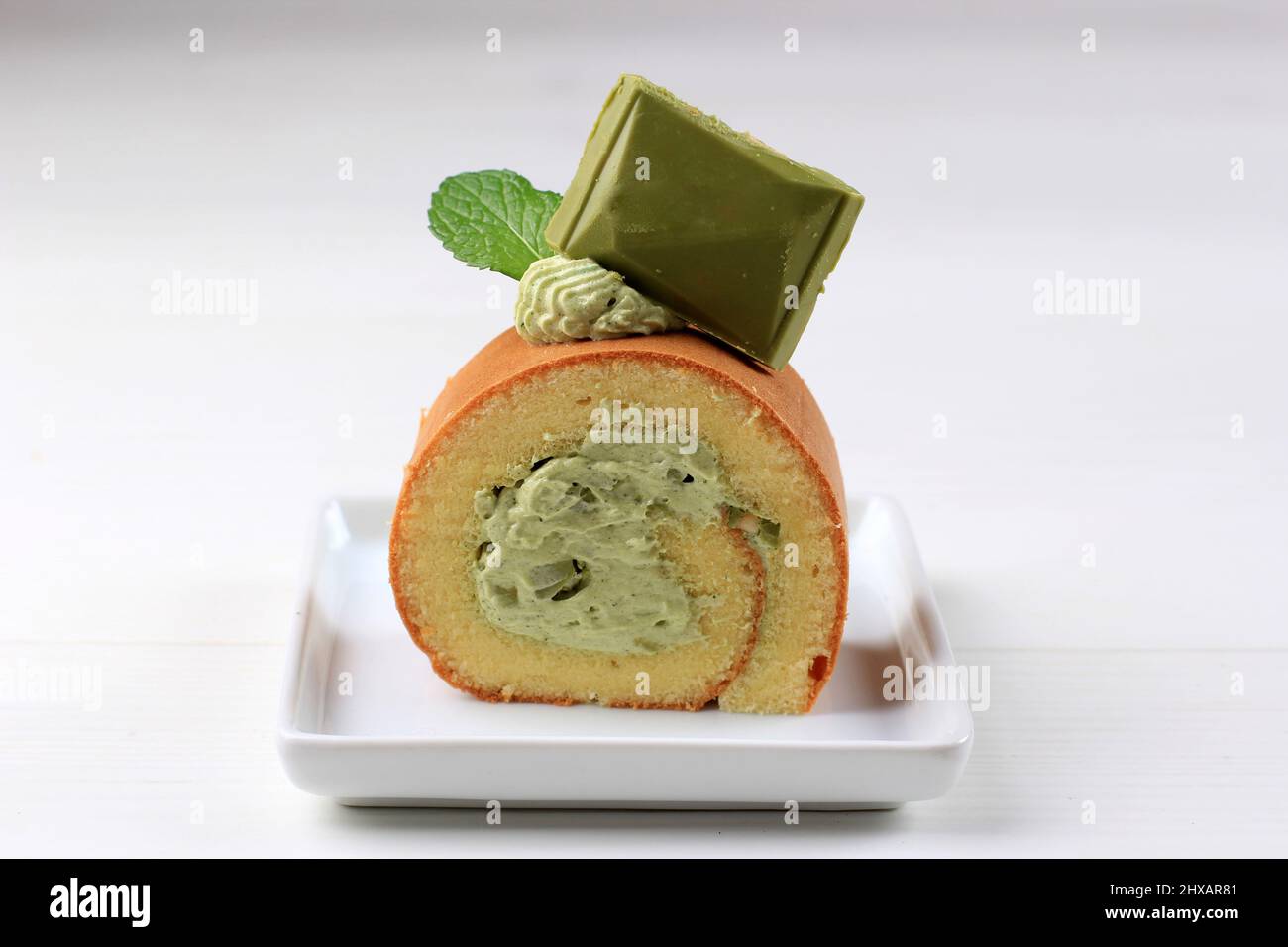 Grüner Tee-Rollkuchen mit Matcha-Schokolade auf der Oberseite, serviert auf weißem Kuchen, weißer Tisch Stockfoto