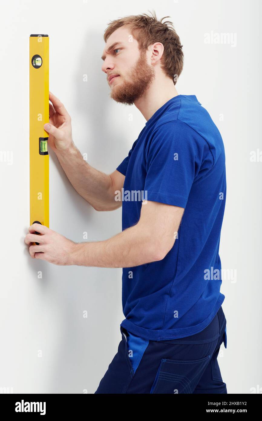 Sicherstellen, dass die Wand waist. Ein unrasierter junger Mann, der eine Ebene benutzt, um sicherzustellen, dass die Wand gerade ist. Stockfoto